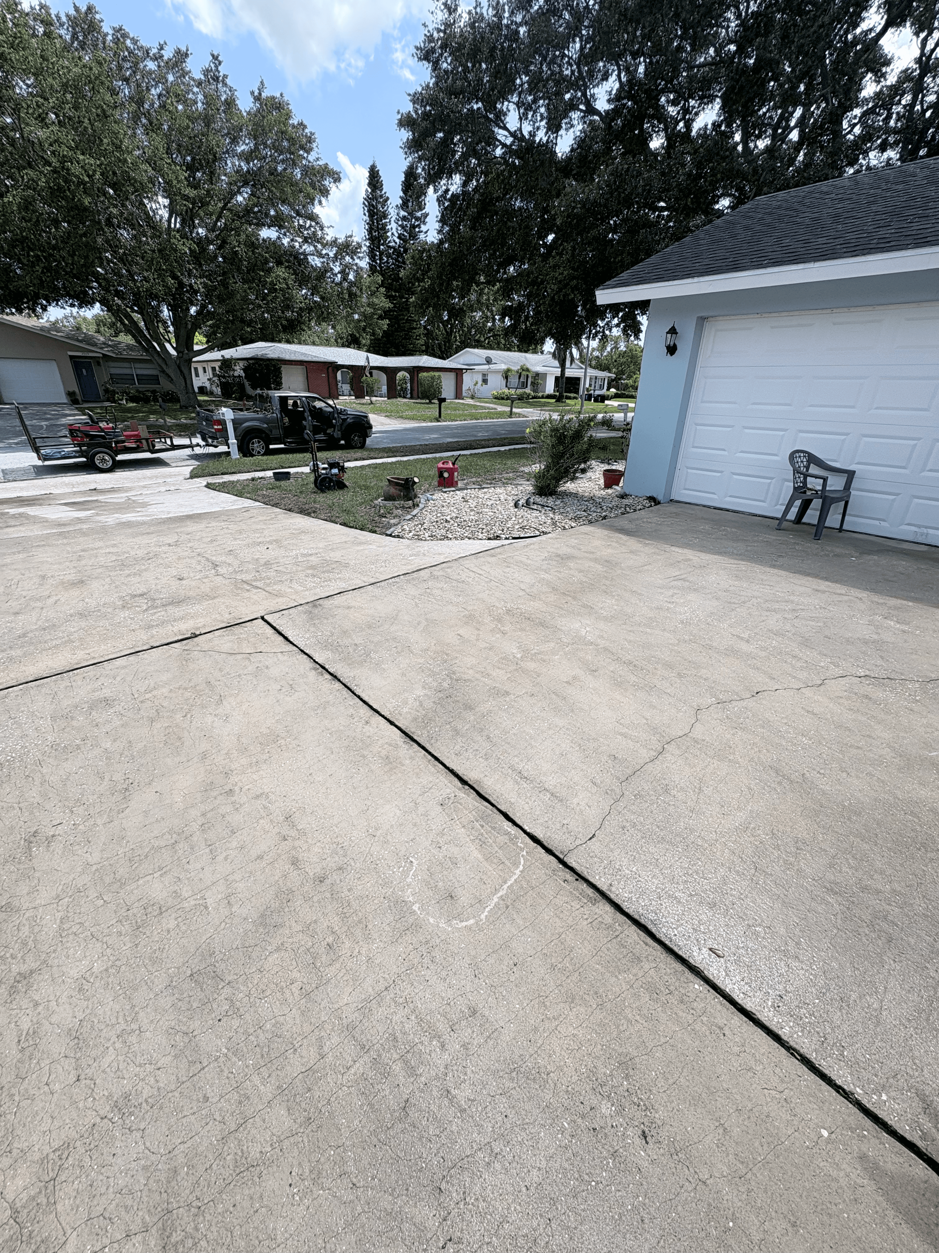 Cracked concrete driveway in front of a blue house with landscaping equipment and a truck.